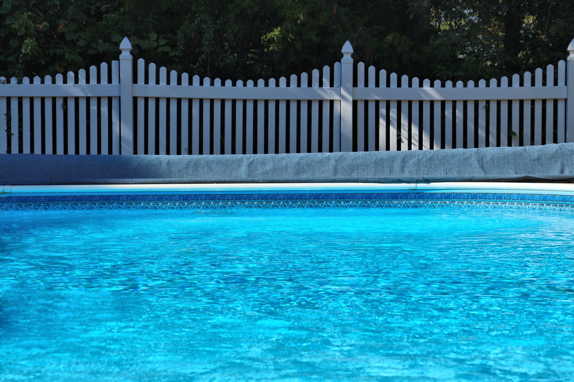 Backyard swimming pool by white vinyl fence and trees